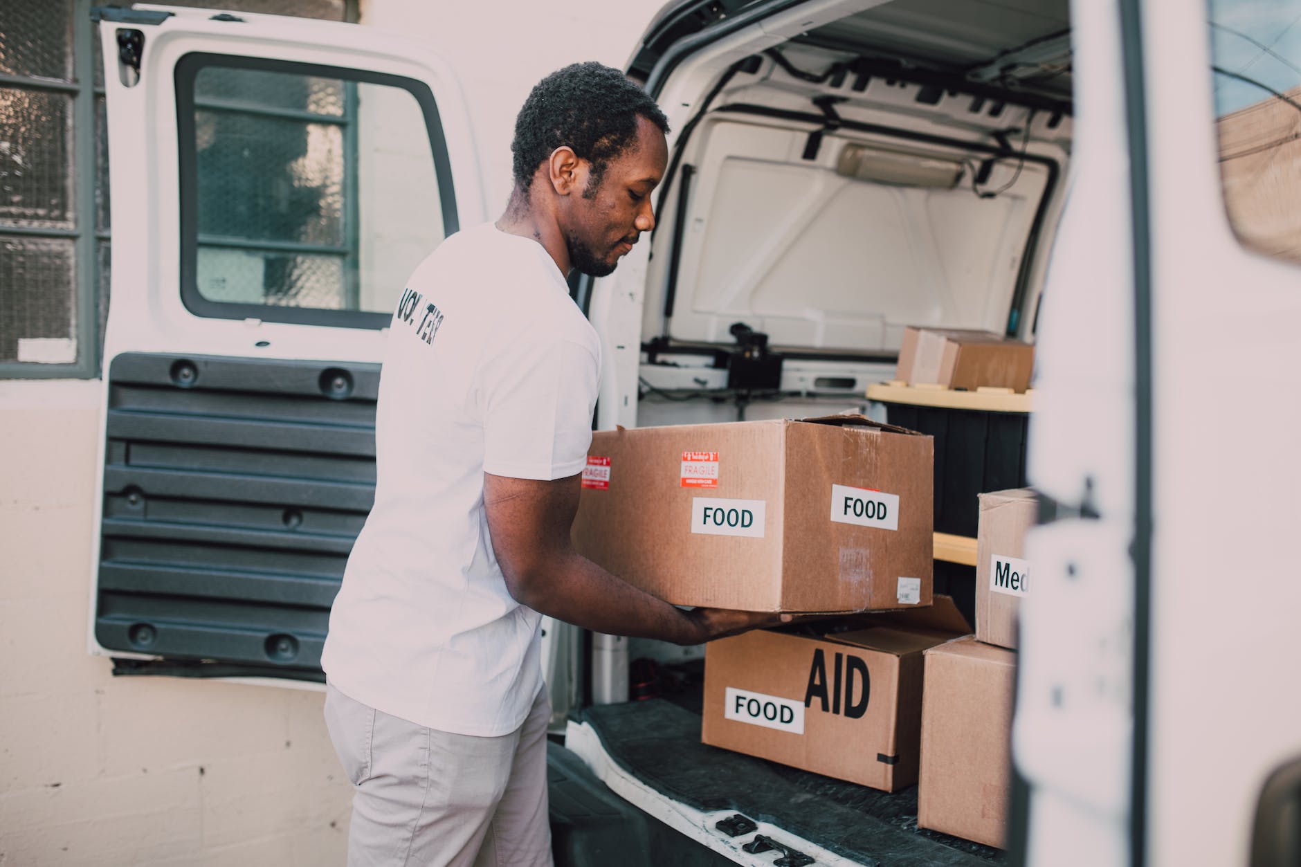 man placing food labelled carboard boxes inside the trunk of a white van