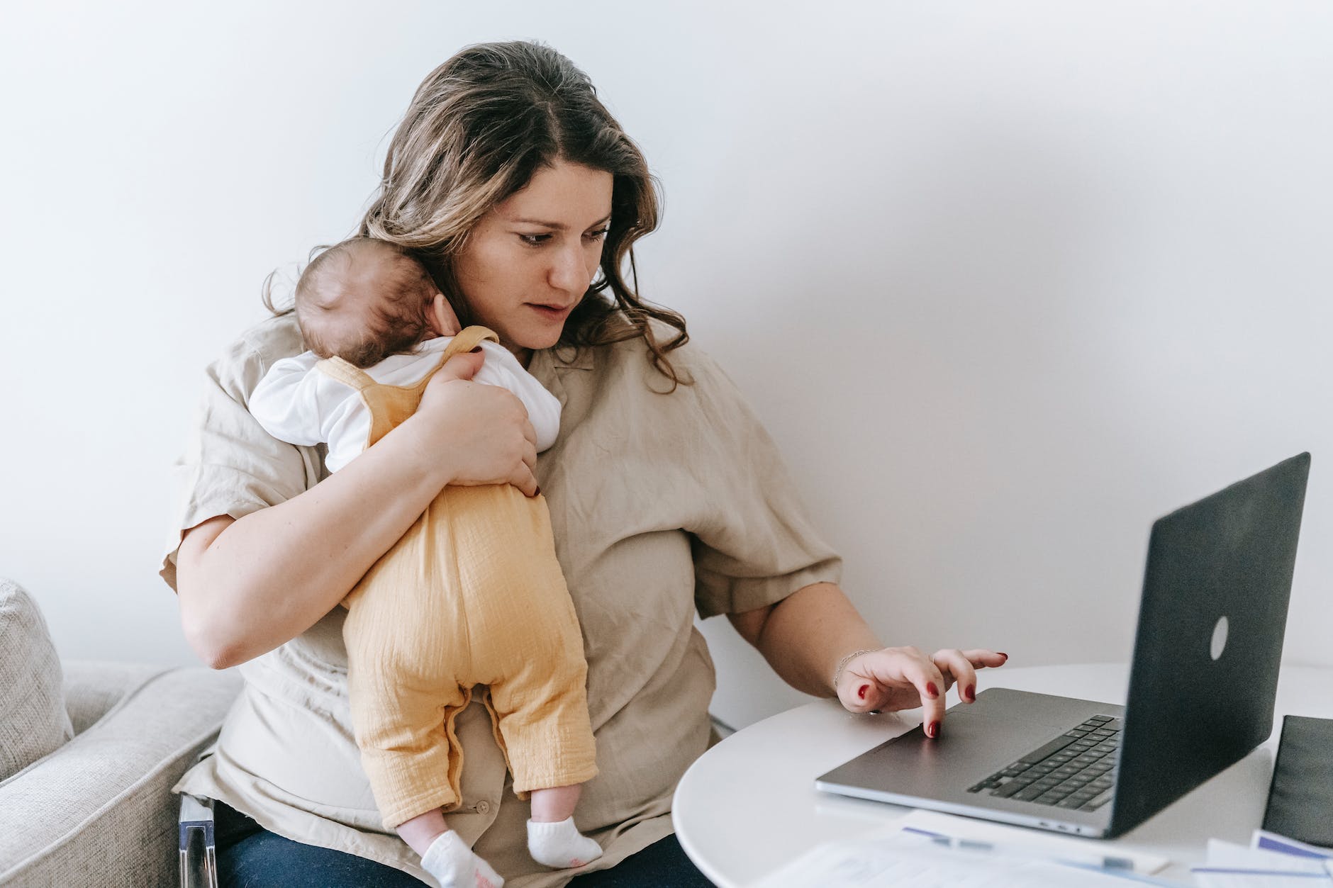 young working mother cuddling baby and using laptop at home